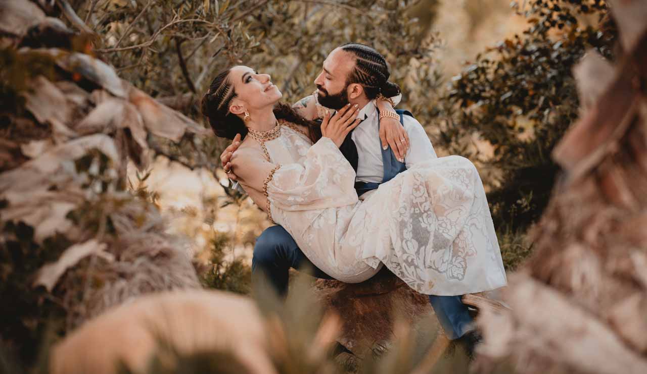 Sposa in braccio allo sposo seduti su un maso nel giardino del Baglio Santa Lucia